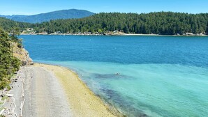 Un paisaje costero con un mar azul cristalino, una playa arenosa y una colina cubierta de bosque al fondo.