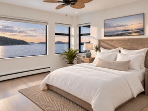 A bedroom with a large bed, a ceiling fan, and a view of a lake.