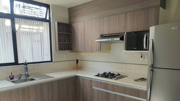 Une cuisine avec des meubles en bois, un réfrigérateur en acier inoxydable, un four à micro-ondes, une cuisinière à gaz et une fenêtre avec des stores.
