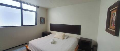 Un dormitorio con cama, mesitas de noche, ventana y lámpara en el techo.