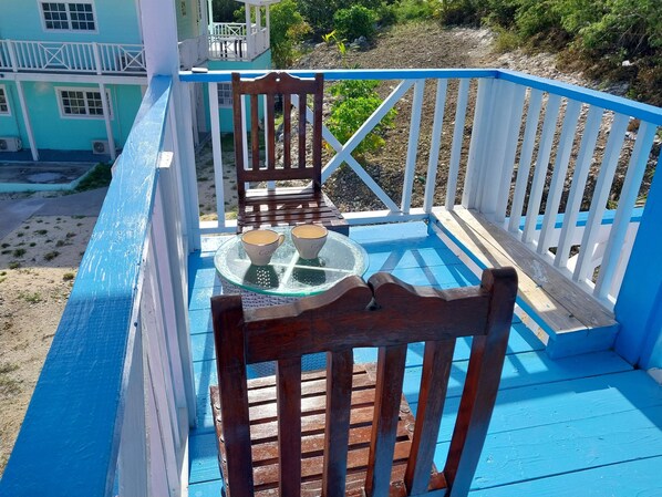 Une terrasse bleue avec une table en verre et deux chaises, donnant sur un jardin.