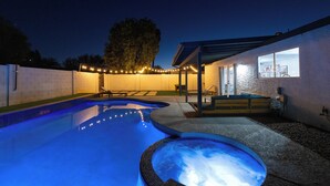 A swimming pool with a hot tub, surrounded by a deck area with lounge chairs and string lights. - MUST SEE! Heated Jacuzzi w/ Pool! Newly Remodeled! Mid-Century Modern Decor!  (Chandler)