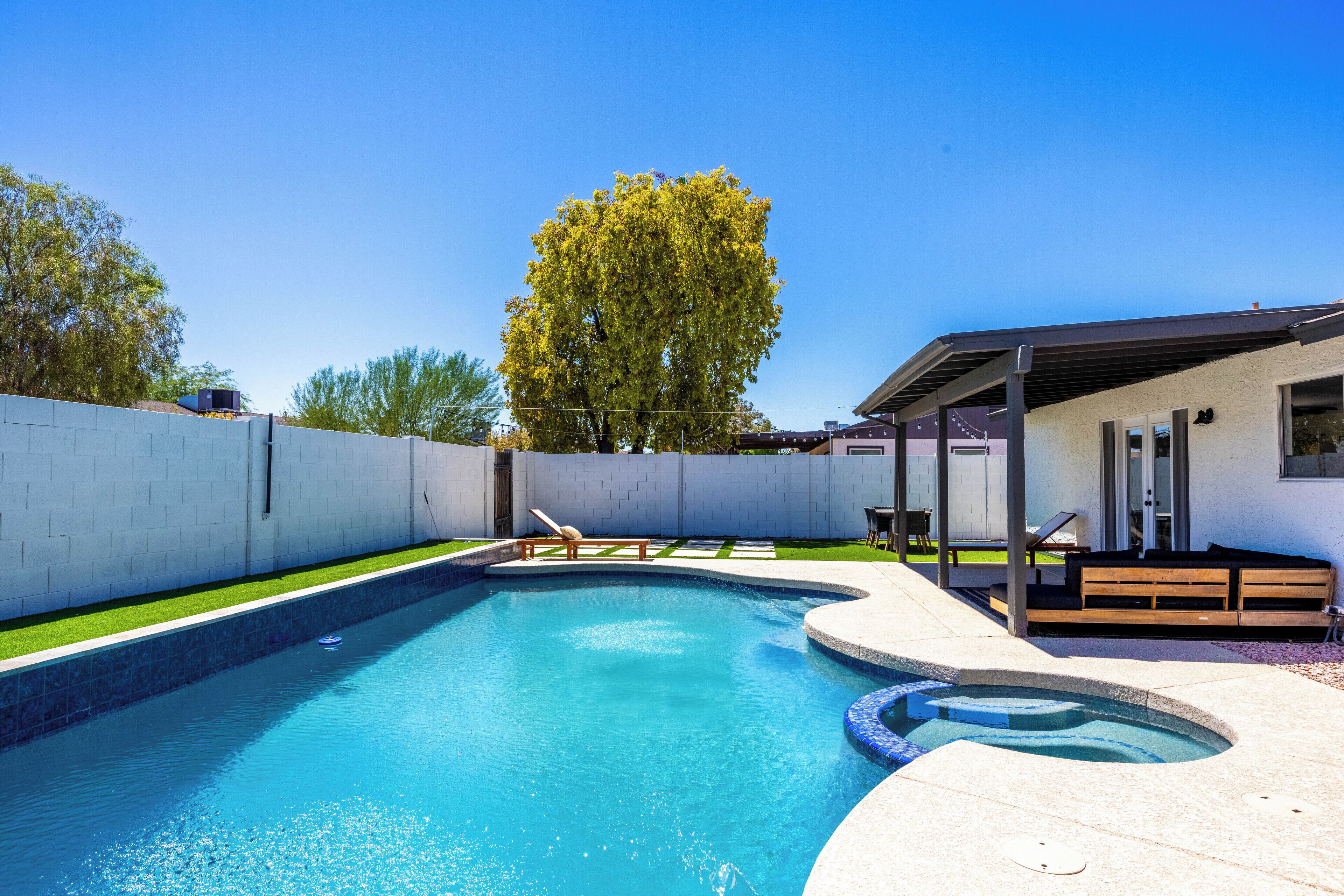 Une piscine au design incurvé, une terrasse en bois et un espace salon couvert.