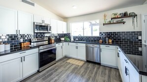 A modern kitchen with white cabinets, black tiled backsplash, stainless steel appliances, and a window providing natural light. - MUST SEE! Heated Jacuzzi w/ Pool! Newly Remodeled! Mid-Century Modern Decor!  (Chandler)
