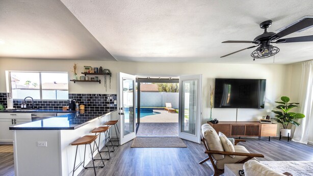 A modern kitchen with a central island, bar stools, and a sliding glass door leading to a patio. - MUST SEE! Heated Jacuzzi w/ Pool! Newly Remodeled! Mid-Century Modern Decor!  (Chandler)