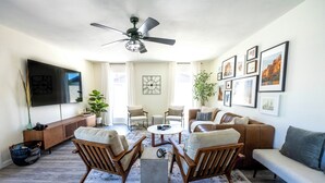 A living room with a sofa, two armchairs, a coffee table, a TV, and framed pictures on the wall. - MUST SEE! Heated Jacuzzi w/ Pool! Newly Remodeled! Mid-Century Modern Decor!  (Chandler)