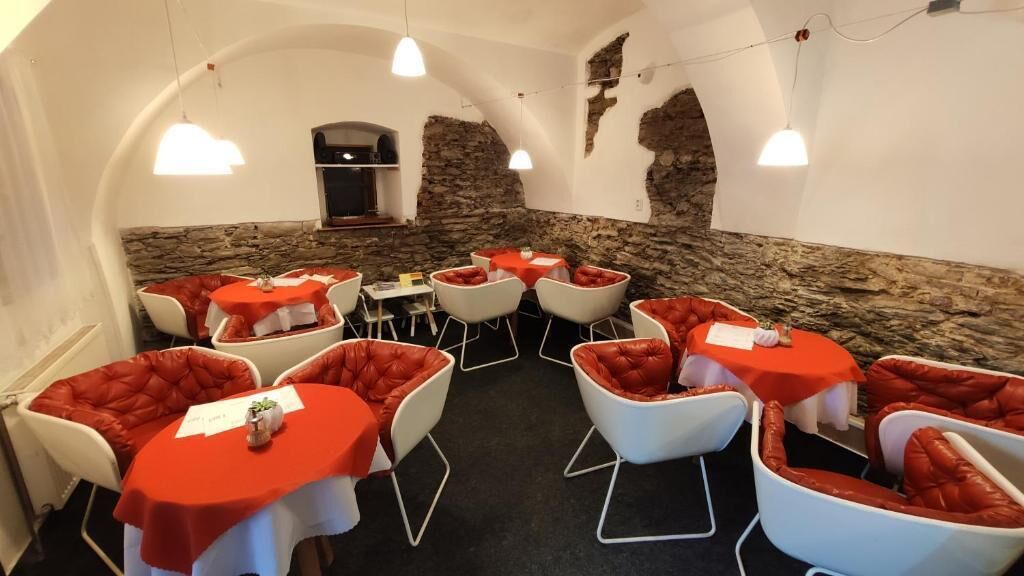 Un restaurante con mesas blancas y sillas rojas acolchadas, con un fondo de pared de piedra.