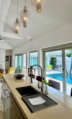 A modern kitchen with a large island, a built-in sink, and a view of a swimming pool.