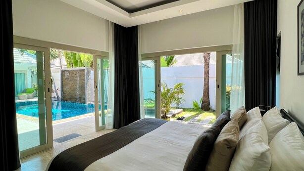 A bedroom with a large bed, a view of a swimming pool, and a sliding glass door leading to an outdoor area.
