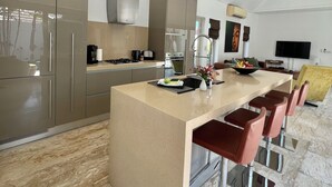 A modern kitchen with stainless steel appliances, a large island with bar stools, and a dining area with a flat-screen TV.