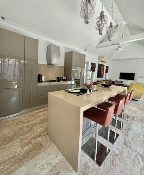 Una cocina moderna con electrodomésticos de acero inoxidable, una isla grande con taburetes de bar y una zona de comedor con televisor de pantalla plana.