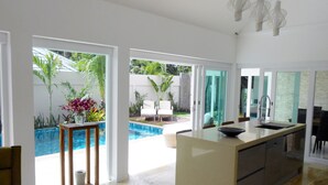 A modern kitchen with a central island, a dining area with chairs, and a view of a swimming pool and garden.