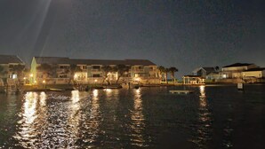 Ein Hotel am Wasserufer mit mehreren Gebäuden, spiegelnder Wasseroberfläche und sichtbarem Mond am Himmel.