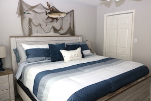 Un dormitorio con cama, mesita de noche, lámpara, puerta y un adorno en la pared.