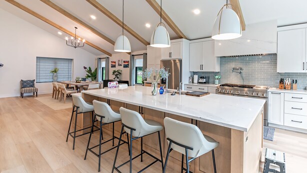 Een moderne keuken met een groot schiereiland, barstoelen, hanglampen en een eethoek met uitzicht.