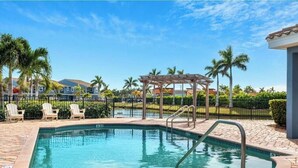 Ein gemeinschaftlicher Pool mit klarem, blauem Wasser, umgeben von einer Ziegelterrasse, Palmen und einem Pergola.