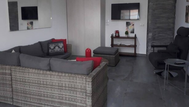 A living room with a sofa, a red ottoman, a small table with a kettle, and a TV mounted on the wall. - Studio In Dbayeh In A Prime Location, Wifi, 38sqm (Dbayeh)