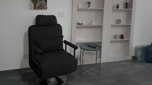 A modern living room with a black armchair, a small round table, and a white shelving unit with various decorative items. - Studio In Dbayeh In A Prime Location, Wifi, 38sqm (Dbayeh)