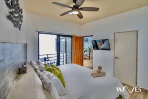 Quarto com cama, ventoinha no teto, televisão e porta de vidro deslizante para uma varanda.