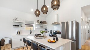 A modern kitchen with white cabinetry, a stainless steel refrigerator, and a central island with bar stools. - Grand Lake View with Outdoor TV, Fireplace, Hot Tub & Game Room Free Attractions Tickets_Cmty Pool (Kimberling City)