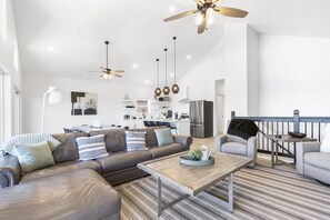 Un salon moderne avec un canapé, des fauteuils, une table basse et une cuisine en arrière-plan.