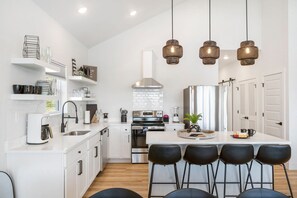 Une cuisine moderne avec des meubles blancs, un îlot central doté de tabourets, un four encastré et des luminaires suspendus.