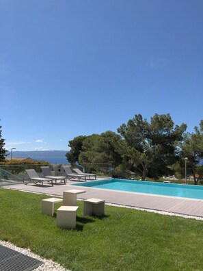 Una piscina con sillas de descanso y un área verde.
