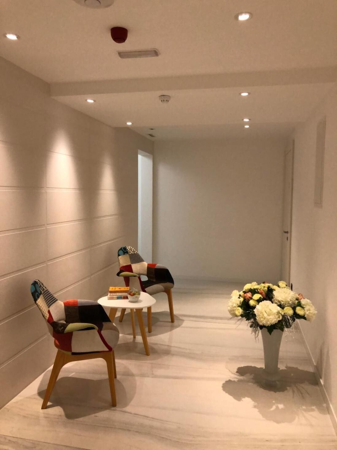 A hallway with two chairs, a small table, and a vase of flowers.