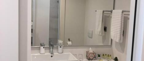 A modern bathroom with a large mirror, two sinks, a toilet, and neatly arranged towels.