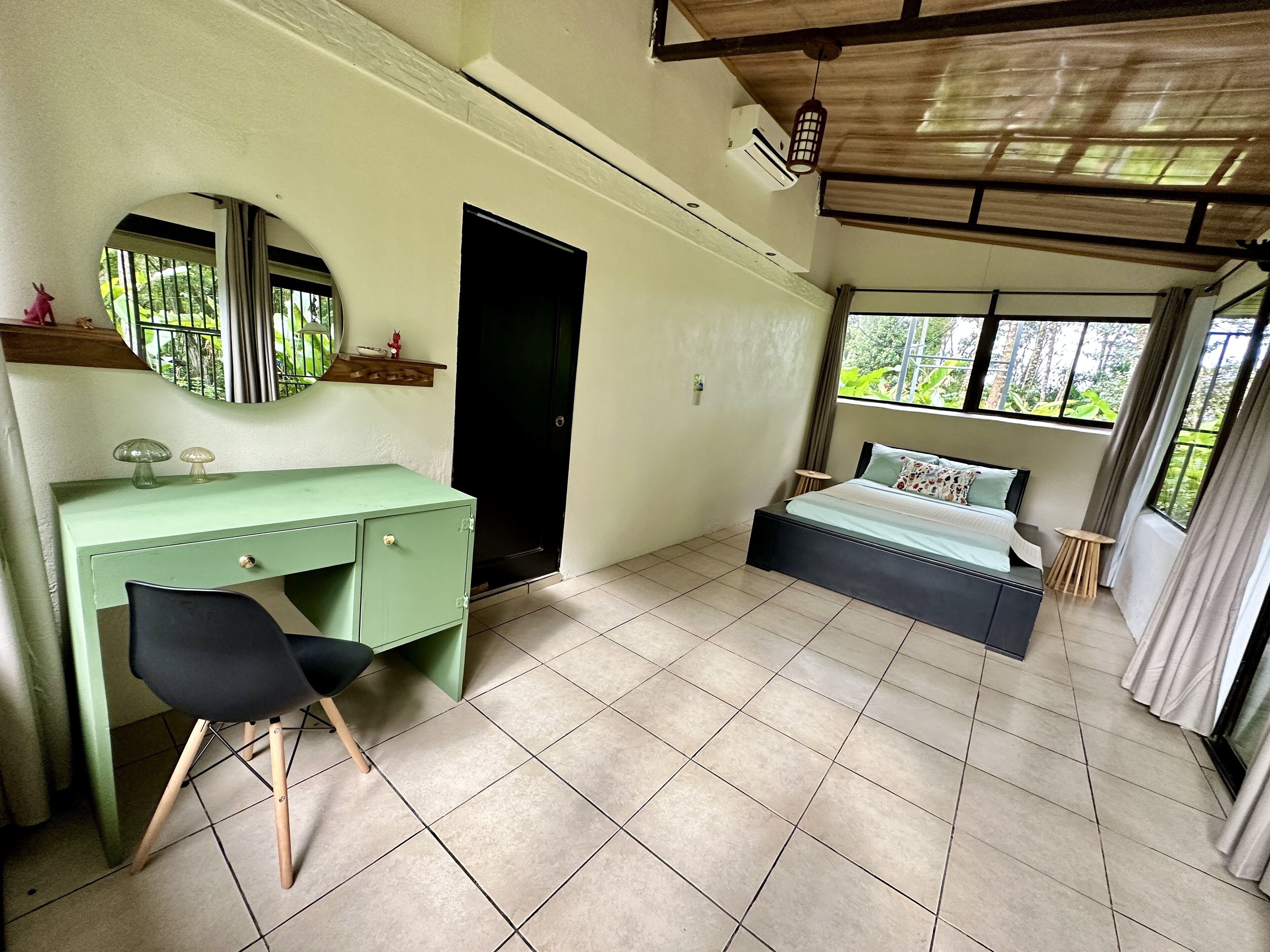 Un dormitorio con una cama, un escritorio, una silla, un espejo, una puerta y una ventana.
