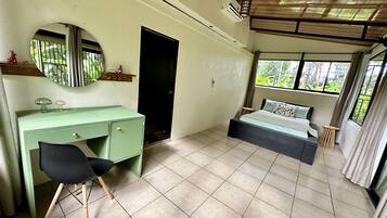 Un dormitorio con una cama, un escritorio, una silla, un espejo, una puerta y una ventana.