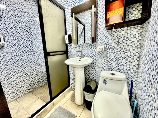 Un baño con lavamanos blanco, inodoro y espejo sobre el lavamanos. Las paredes están revestidas con un diseño azul y blanco.