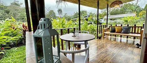 Un patio al aire libre con una mesa redonda de madera, una silla blanca, un farol y un banco con cojines.