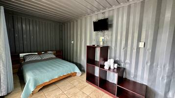 A room with a bed, a TV mounted on the wall, and a wooden cabinet with towels.
