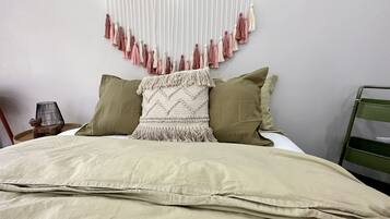 A neatly made bed with a beige blanket, two pillows, and a decorative macramé wall hanging.