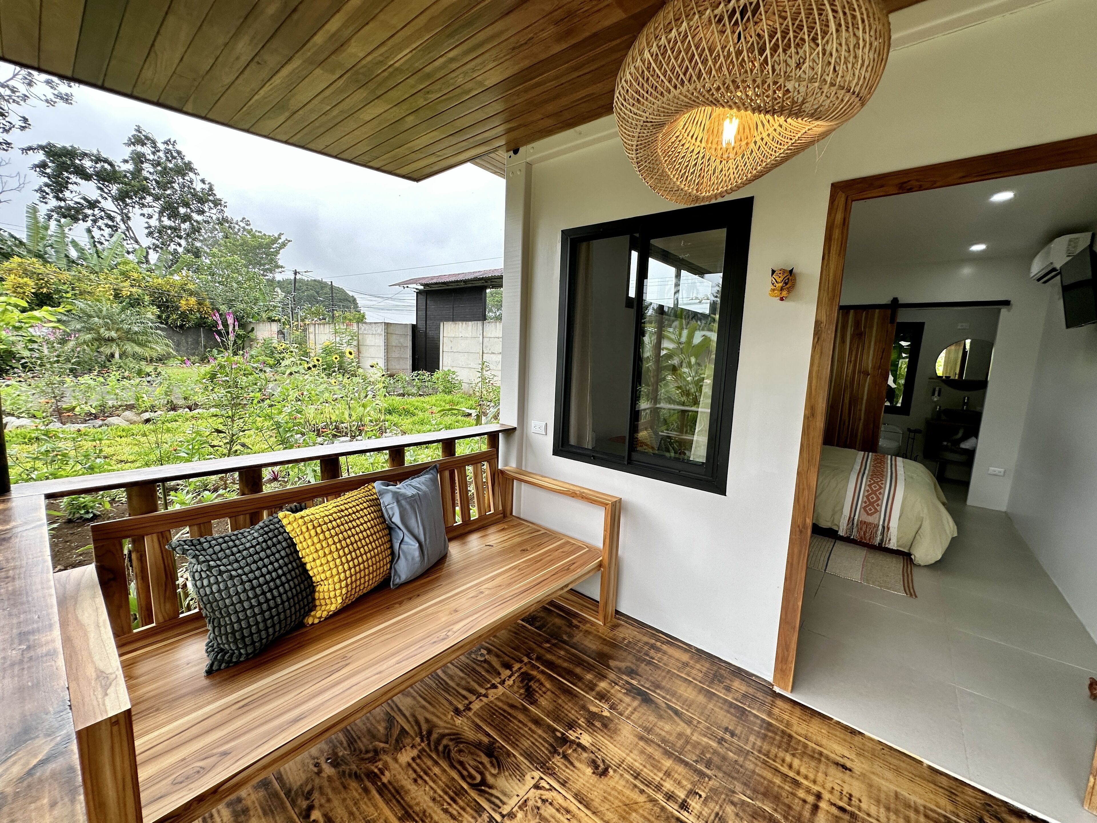 Un banco de madera con cojines, una lámpara de fibra y vista a un jardín por una ventana.