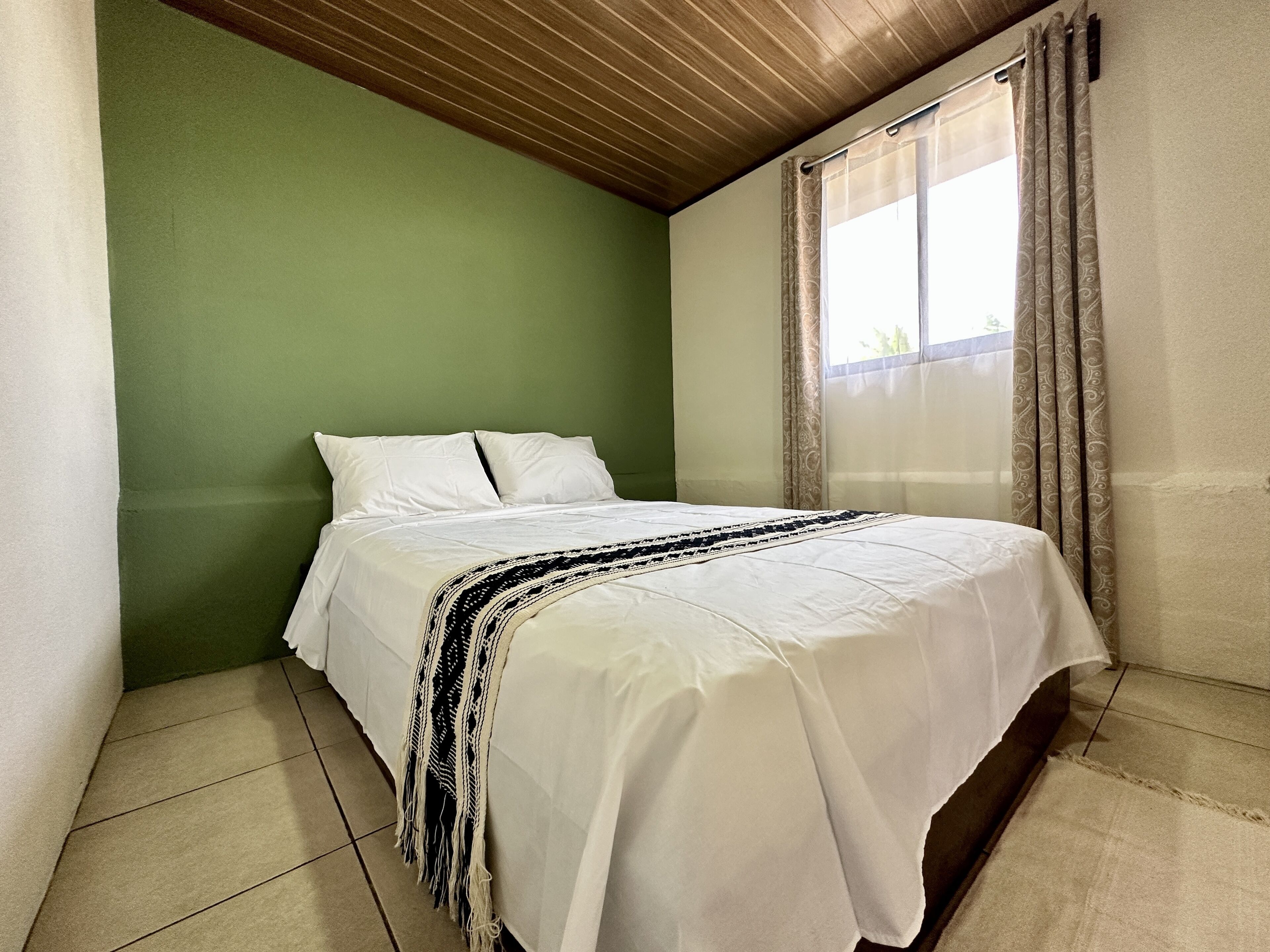 Una cama bien hecha en una habitación con paredes verdes y techo de madera.