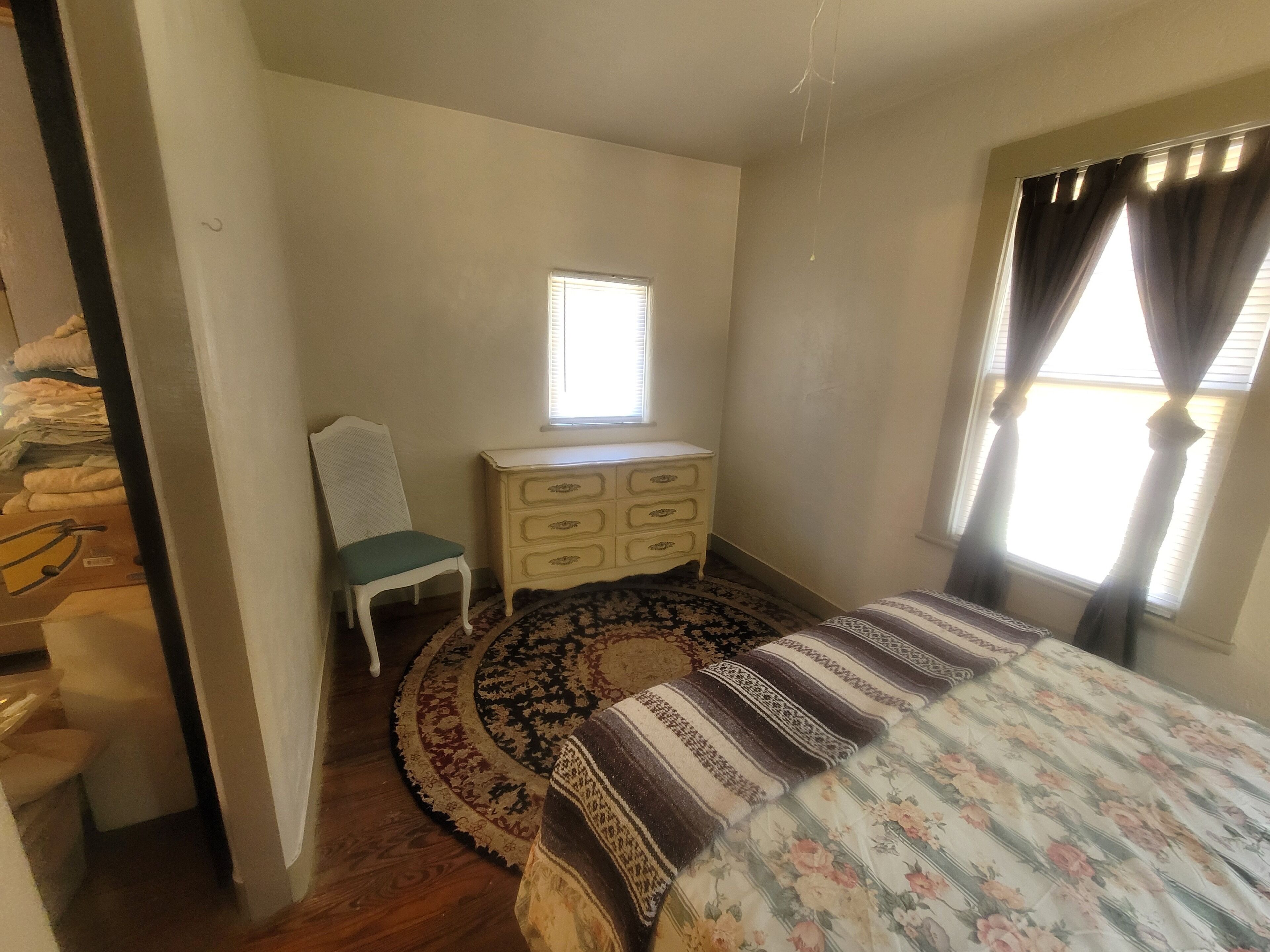 A bedroom with a bed, a dresser, a chair, a window with curtains, and a patterned rug.