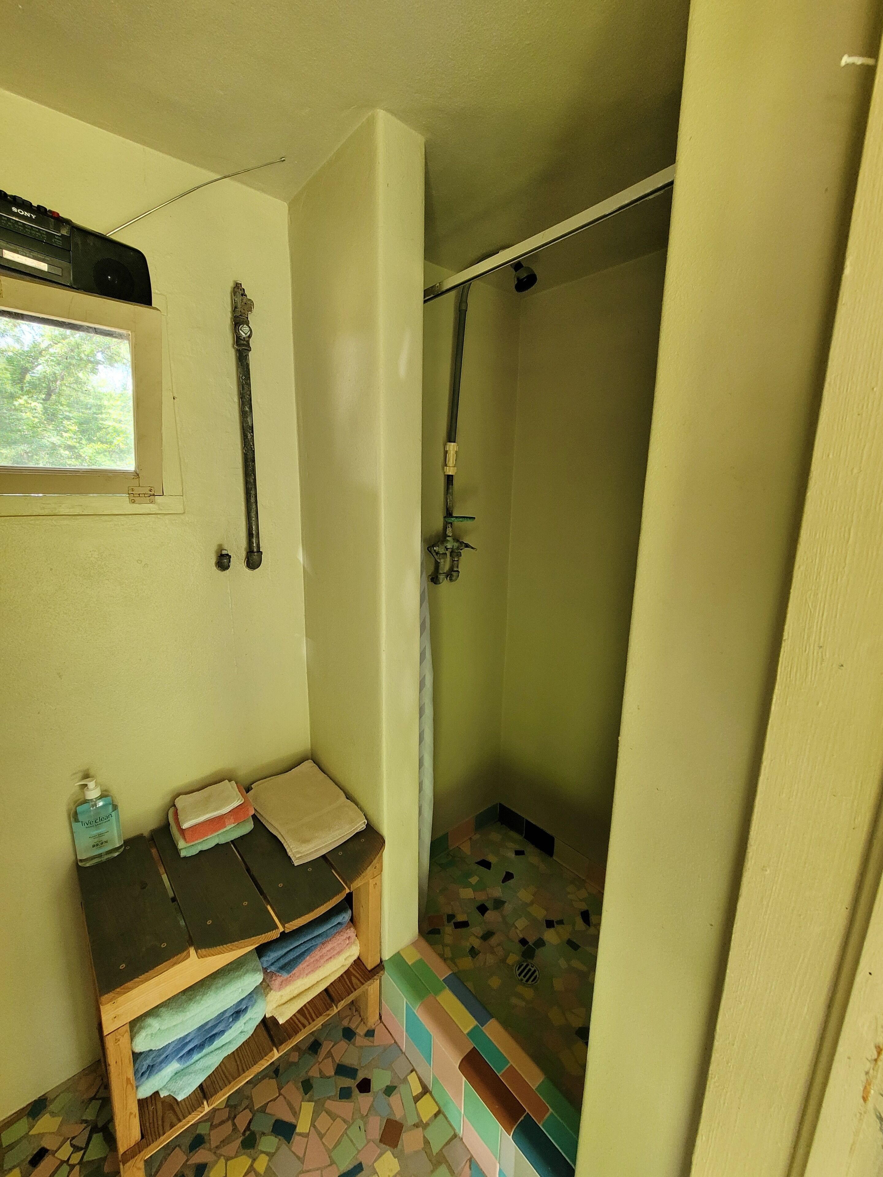 A bathroom with a shower, a window, a sink, and a shelf with towels and toiletries.