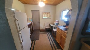 A compact kitchen with a refrigerator, a wooden table, a chair, and a window with curtains.
