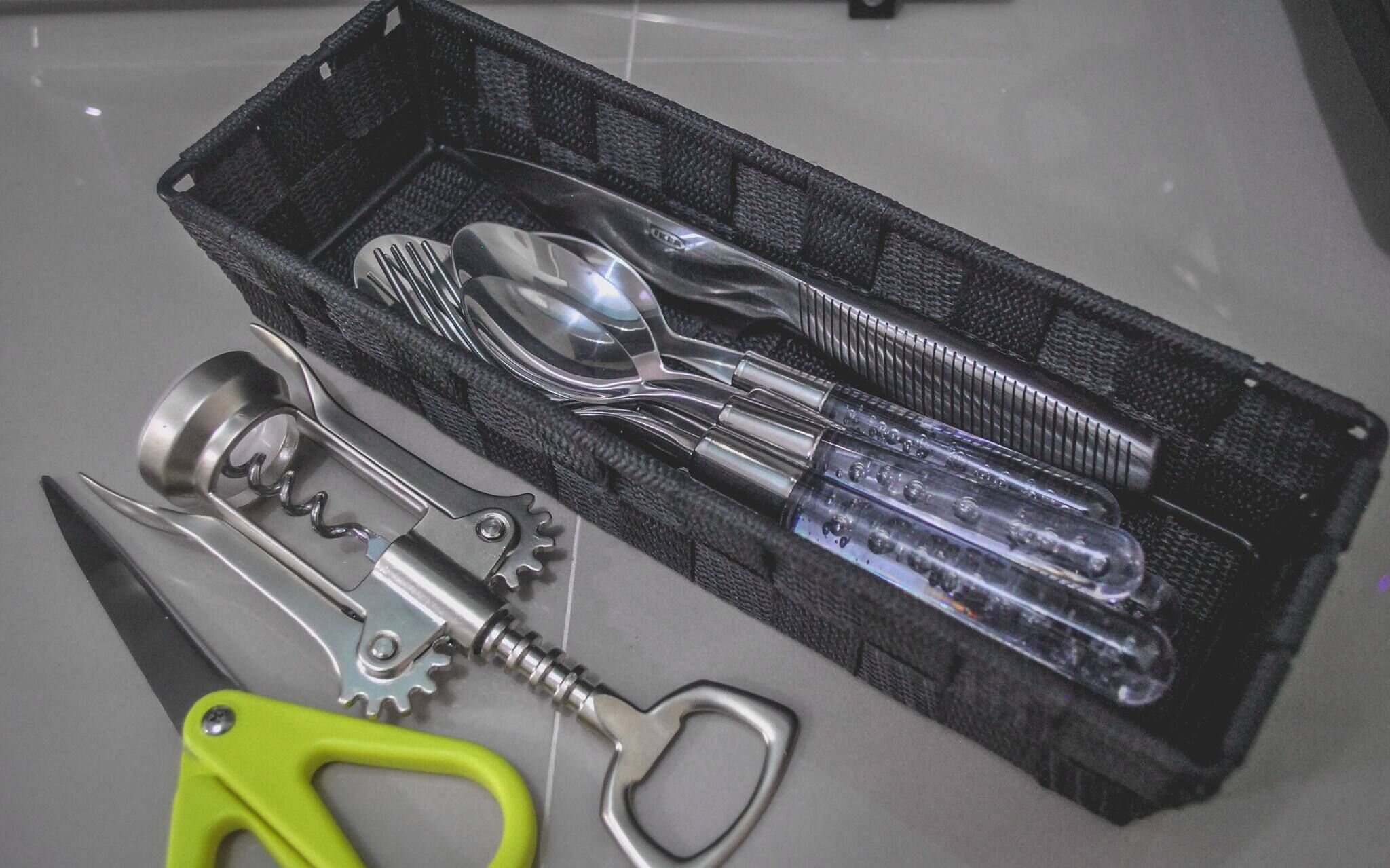 Un ensemble d’ustensiles de cuisine comprenant une cuillère, une fourchette et un couteau, le tout rangé dans un étui noir en maille.