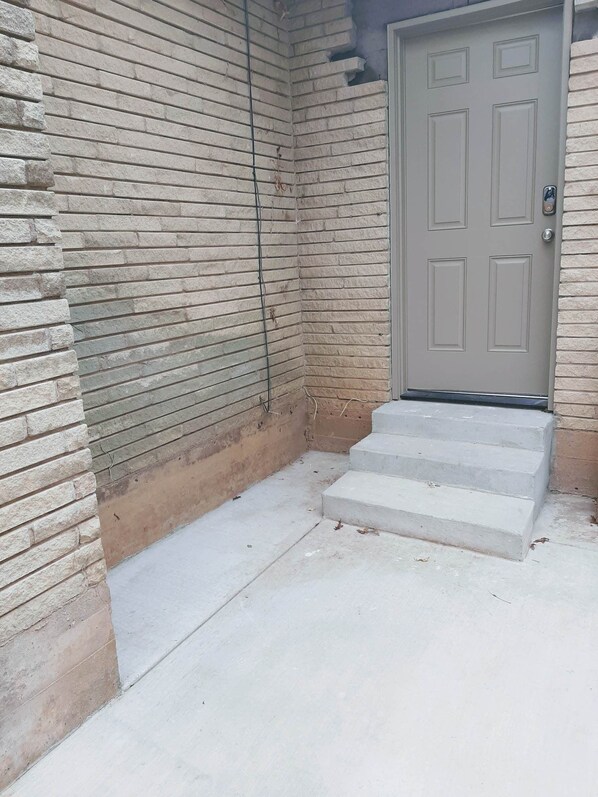 A building entrance with a grey door and concrete steps leading up to a porch.