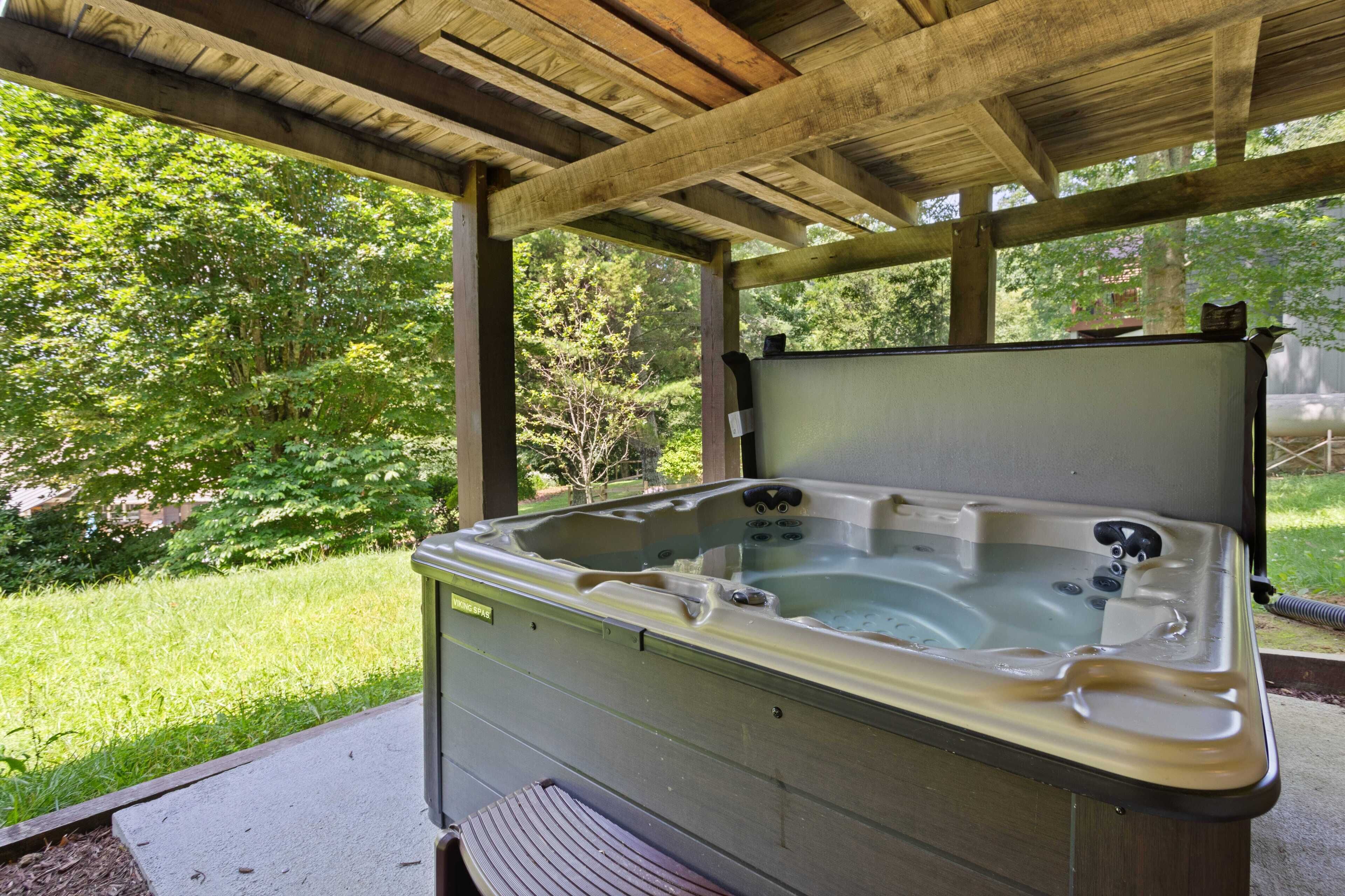 Un jacuzzi bajo una pérgola de madera, con un césped y árboles al fondo.