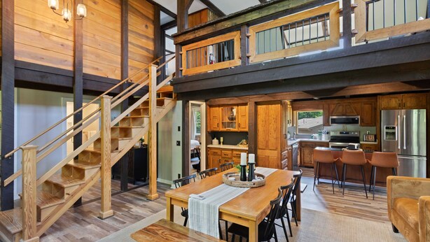A spacious kitchen with modern appliances, a dining area with a wooden table and chairs, and a wooden staircase leading to an upper level. - Walk to Downtown Banner Elk | Hot Tub, Movie Room & Game Room | Sleeps 17 (Banner Elk)