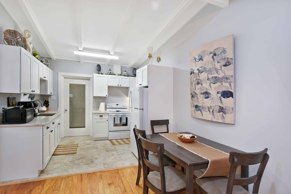 A compact kitchen with white cabinets, a dining table with chairs, and a painting on the wall.