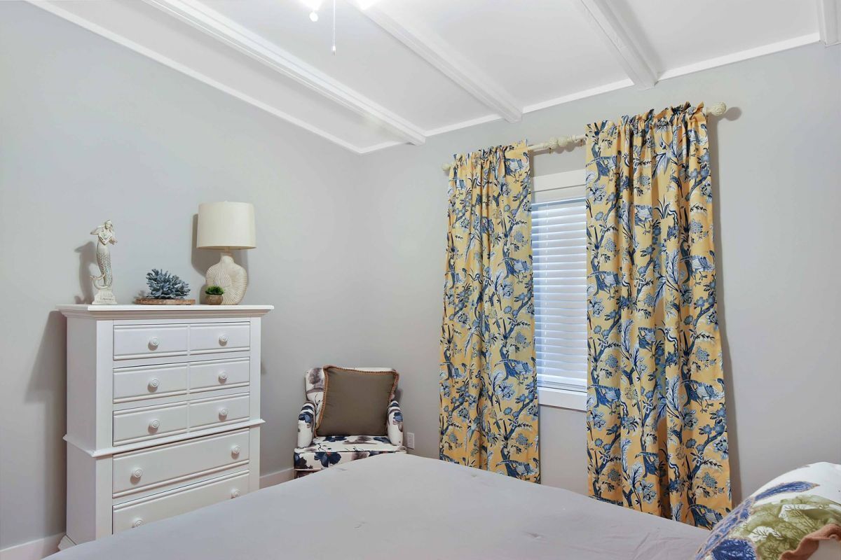 A bedroom with a bed, a dresser, a chair, and a window with curtains.