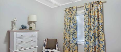 A bedroom with a bed, a dresser, a chair, and a window with curtains.