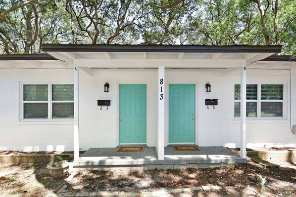 A white building with two green doors, numbered 813, and a covered porch with steps.
