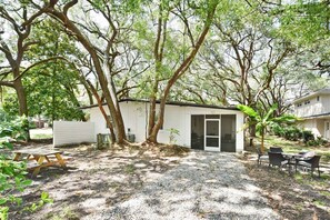 A small, single-story building with a white exterior, surrounded by trees and a gravel yard.