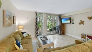 Un salon comprenant un canapé, une table basse, un téléviseur et une porte-fenêtre coulissante donnant sur un balcon.